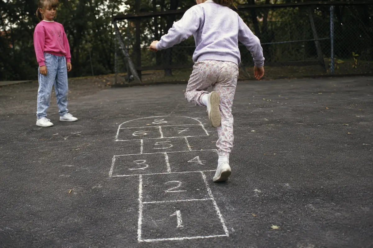 Two children playing hopscotch, one of the playground games played before smartphones