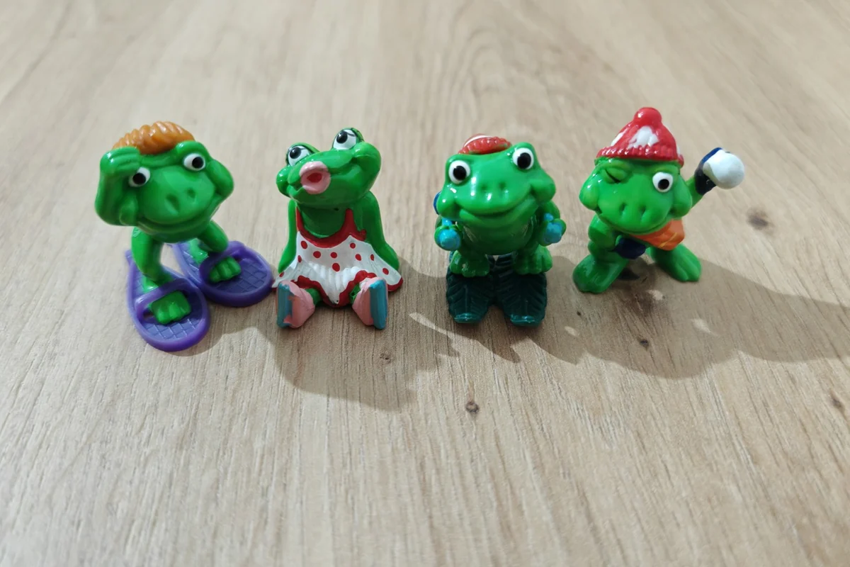 Four green Kinder figures from the Ranoplà frog series, with snowshoes, skates, skis and a snowball